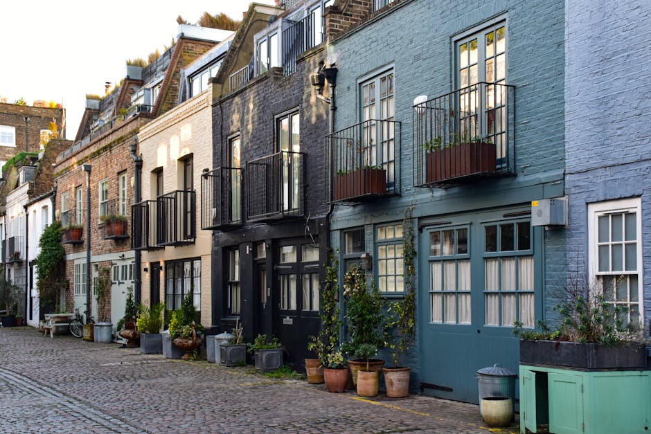 A row of traditional terraced houses with facades painted in shades of black, cream, and blue, situated along a narrow cobblestone street. Each building features small balconies with black metal raili